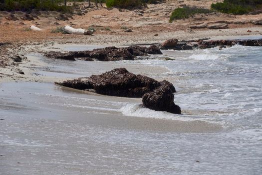 Waves against big rocks on the shore of the beach, turquoise water. Mediterranean Sea. Balearic Islands, sandy beach,
