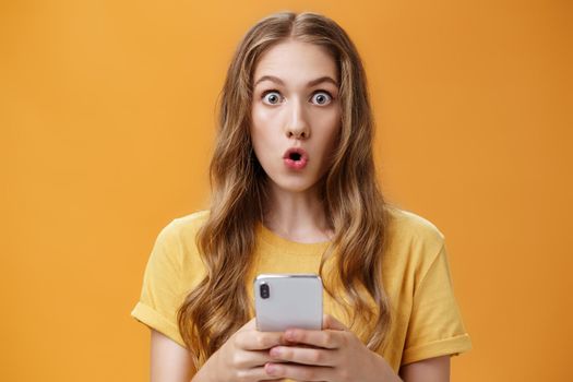 Lifestyle. Close-up shot of impressed astonished cute young girl with makeup on and natural wavy hair folding lips in wow sound from amazement holding smartphone reacting to cool new device or app.