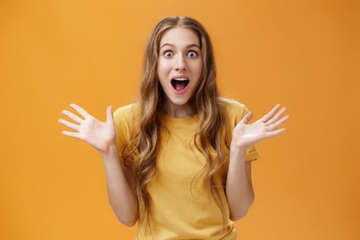 Impressed excited girl describing feelings sharing positive impression gesturing with palms during talk open mouth from amazement and oy communicating lively over orange background. Body language concept