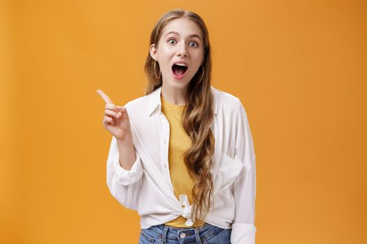 Your jaw will drop after this copy space. Portrait of charismatic young good-looking stylish girl with wavy hair open mouth widely pointing at upper left corner showing awesome place or product.