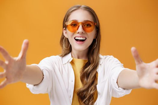 Lifestyle. Girl reaching to camera to hug or grab thing looking forward with broad grin and excited desiring expression wanting hold in hands new product posing amused and happy over orange background.