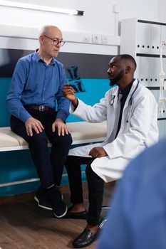 Practitioner physician doctor holding lungs radiography of retired old man discussing sickness symptoms explaining healthcare treatment in hospital office. Senior patient having medical appointment