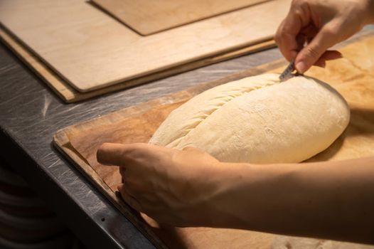 Close-up of a baker's female hands cutting a loaf of dough into a loaf of bread with a blade before baking in the oven. Craft craft bread production.