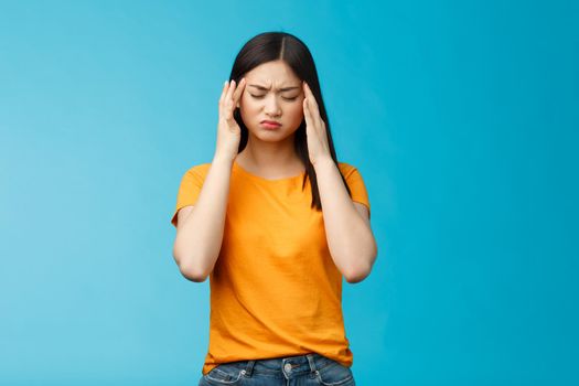 Distressed tired asian woman dark haircut cringe touch temples, suffer huge migraine need painkillers, painful headache, feel dizzy, stand blue background intense drained. Copy space