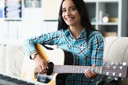 Portrait of happy young woman playing on guitar in living room at home, spend free time learning new song on musical instrument. Music, hobby, joy concept
