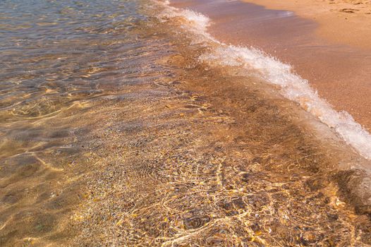 Wave of foam and white sand on the beach. Crystal clear sea wave on a sandy beach photo background. Golden coral beach sand with sea wave. Seaside exotic island banner with place for text