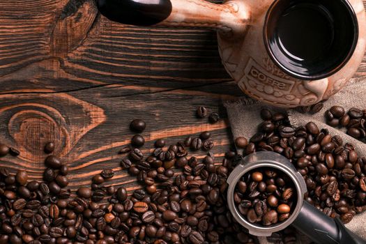 Old coffee cup and turk with roasted beans on a wooden table. Vintage aroma concept on dark background.