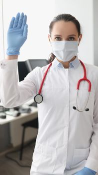 Portrait of professional medical worker in face mask wave hello lifting hand in glove. Full protection at work in clinic. Virus spread, medicine concept