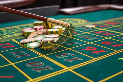 Close up of gambling chips on a green table in casino. Croupier collects chips using stick