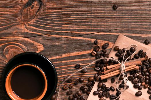 Coffee beans, cinnamon sticks and cup of brewed coffee on rustic wooden table, view from above with space for text. Still life. Mock-up. Flat lay