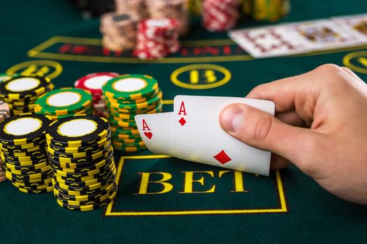 Close-up of male poker player lifting the corners of two cards aces at green casino table with aces