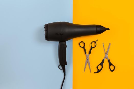 Styling hair with scissors, dryer and tools in barbershop on blue and yellow paper background. Top view. Copy space. Flat lay. Still life. mock-up
