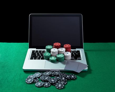 Image of casino chips and cards on a keyboard notebook at green table. Concept for online gambling, poker, virtual casino.