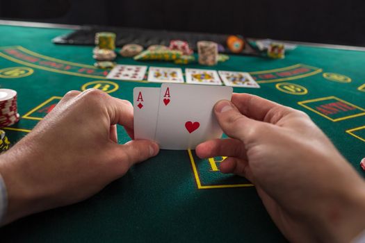 Close-up of male poker player lifting the corners of two cards aces at green casino table with aces