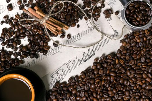 Coffee beans, cinnamon sticks and cup of brewed coffee on sheet music background, view from above with space for text. Still life. Mock-up. Flat lay