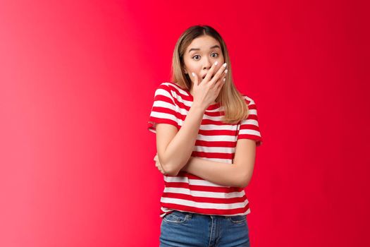 Shocked asian blond girl feel empathy hear shocking news gasping, woman drop jaw cover opened mouth astonished, gossiping juicy rumours, stand red background surprised and impressed.