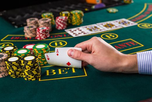 Close-up of male poker player lifting the corners of two cards aces at green casino table with aces