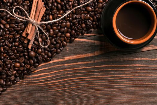 Coffee beans, cinnamon sticks and cup of brewed coffee on rustic wooden table, view from above with space for text. Still life. Mock-up. Flat lay