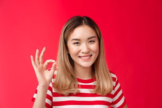 Close-up friendly satisfied carefree young asian blond girl show approval judgement sign okay ok, agree plan good smiling broadly like your idea satisfied great choice, stand red background glad.