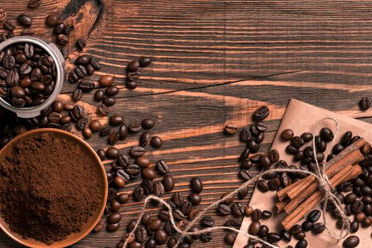 Coffee beans, cinnamon sticks and ground coffee on rustic wooden table, view from above with space for text. Still life. Mock-up. Flat lay