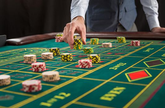 Picture of a green table and betting with chips. Man hand over casino chips on roulette table. Close up