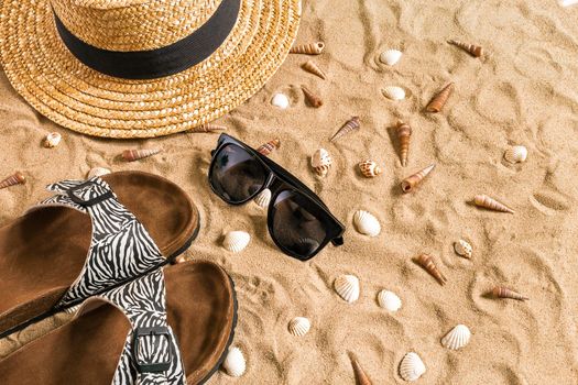 Summer beachwear, flip flops, hat, sunglasses and seashells on sand beach. Top view. Copy space. Still life mockup flat lay