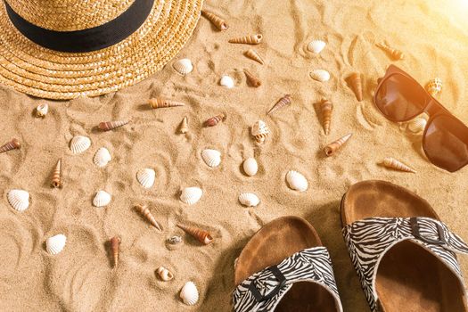 Summer beachwear, flip flops, hat, sunglasses and seashells on sand beach. Top view. Copy space. Sun flare