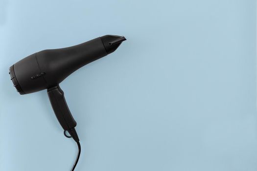 Black hair dryer on blue paper background. Top view. Copy space. Flat lay. Still life. Mockup