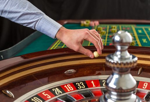 Roulette wheel and croupier hand with white ball in casino close up details