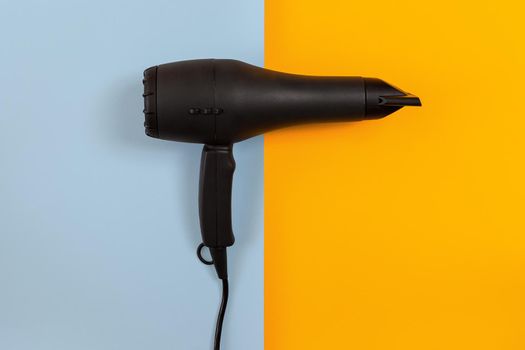 Black Hair dryer on blue and orange background. Top view. Still life. Flat lay. Copy space