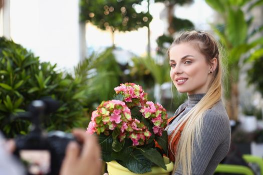 Portrait of beautiful blonde florist studio worker record promotion for botanical store. Female posing with fresh blooming flowers. Shop, sell, ad concept