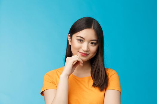 Close-up coquettish good-looking asian young modern woman curiously listen interesting story, smirking relaxed gaze camera, touch chin thoughtful, intrigued stand blue background.