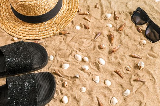 Summer beachwear, flip flops, hat, sunglasses and seashells on sand beach. Top view. Copy space