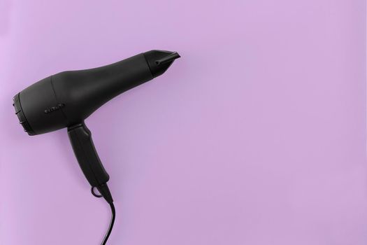 Black hair dryer on lilac paper background. Top view. Copy space. Flat lay. Still life. Mockup