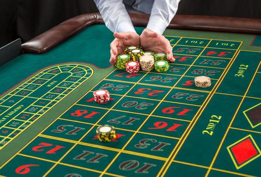 Picture of a green table and betting with chips. Man hand over casino chips on roulette table. Close up