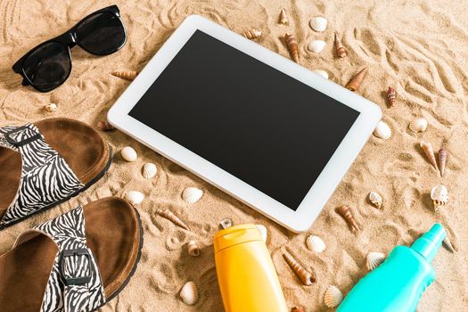 Summer flip-flops, tablet, sunglass and seashell on sand. With place for your text. Top view. Copy space