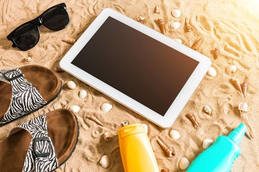 Summer flip-flops, tablet, sunglass and seashell on sand. With place for your text. Top view. Copy space. Sun flare