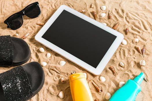Summer flip-flops, tablet, sunglass and seashell on sand. With place for your text. Top view. Copy space