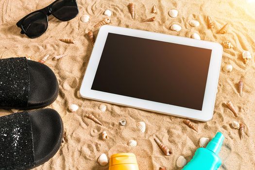Summer flip-flops, tablet, sunglass and seashell on sand. With place for your text. Top view. Copy space. Sun flare