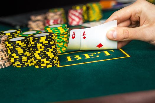 Close-up of male poker player lifting the corners of two cards aces at green casino table with aces