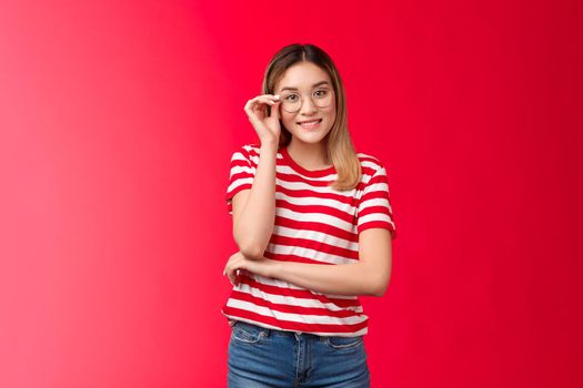 Cheerful geeky cute blond asian female programmer wear glasses smiling joyfully discuss it innovations during conference stand pleased red background, touch eyewear rim grinning pleased.