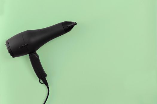 Black hair dryer on green paper background. Top view. Copy space. Flat lay. Still life. Mockup