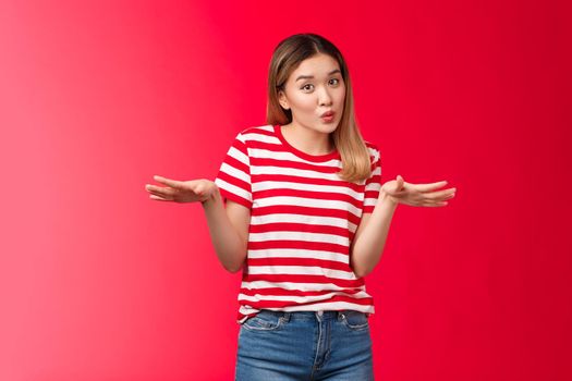 Cute chill asian blond college girl talking girlfriends discussing smooth cool party folding lips cute spread hands sideways gesturing casually, relaxed friendly pose, red background.