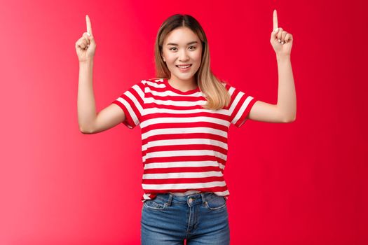 Hey up we go. Cheerful good-looking young asian girl pointing hands up, showing promotion smiling cheerful, female model propose good place hang advertisement, standing red background.