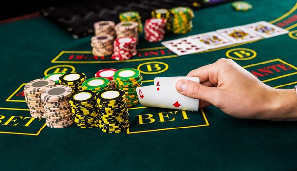 Close-up of male poker player lifting the corners of two cards aces at green casino table with aces