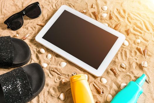 Summer flip-flops, tablet, sunglass and seashell on sand. With place for your text. Top view. Copy space. Sun flare