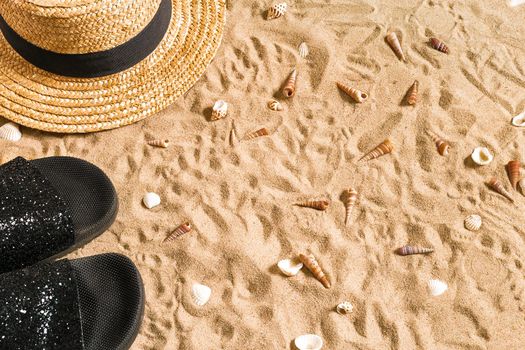 Summer beachwear, flip flops, hat and seashells on sand beach. Top view. Copy space