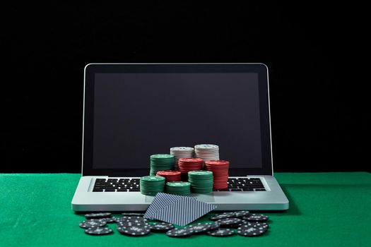 Image of casino chips and cards on a keyboard notebook at green table. Concept for online gambling, poker, virtual casino.