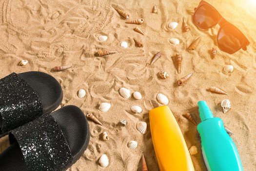 Black flip-flops and sunglass, seashell on sand. With place for your text. Top view. Copy space. Sun flare