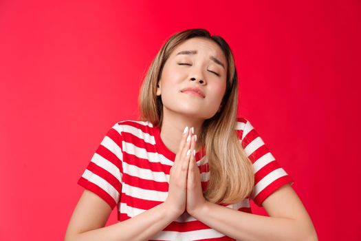 Close-up silly hopeful asian girl blond hairstyle, asking god help, hold hands pray, supplicating raise head up closed eyes, making wish, anticipating miracle, pleading lord dream come true.